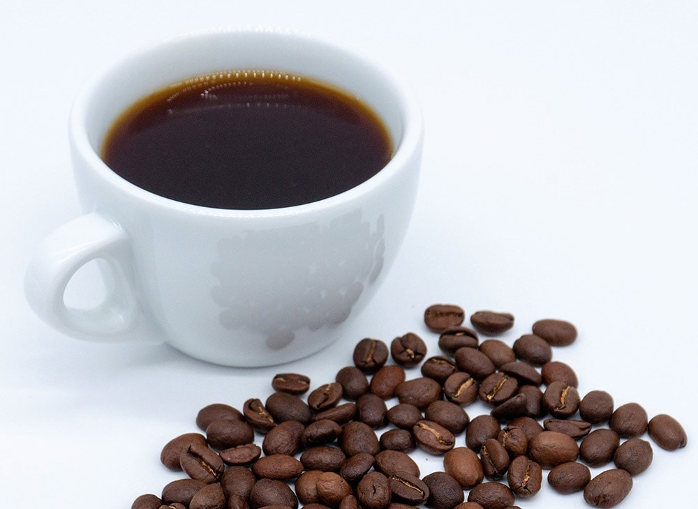 Cup of brewed coffee surrounded by roasted coffee beans