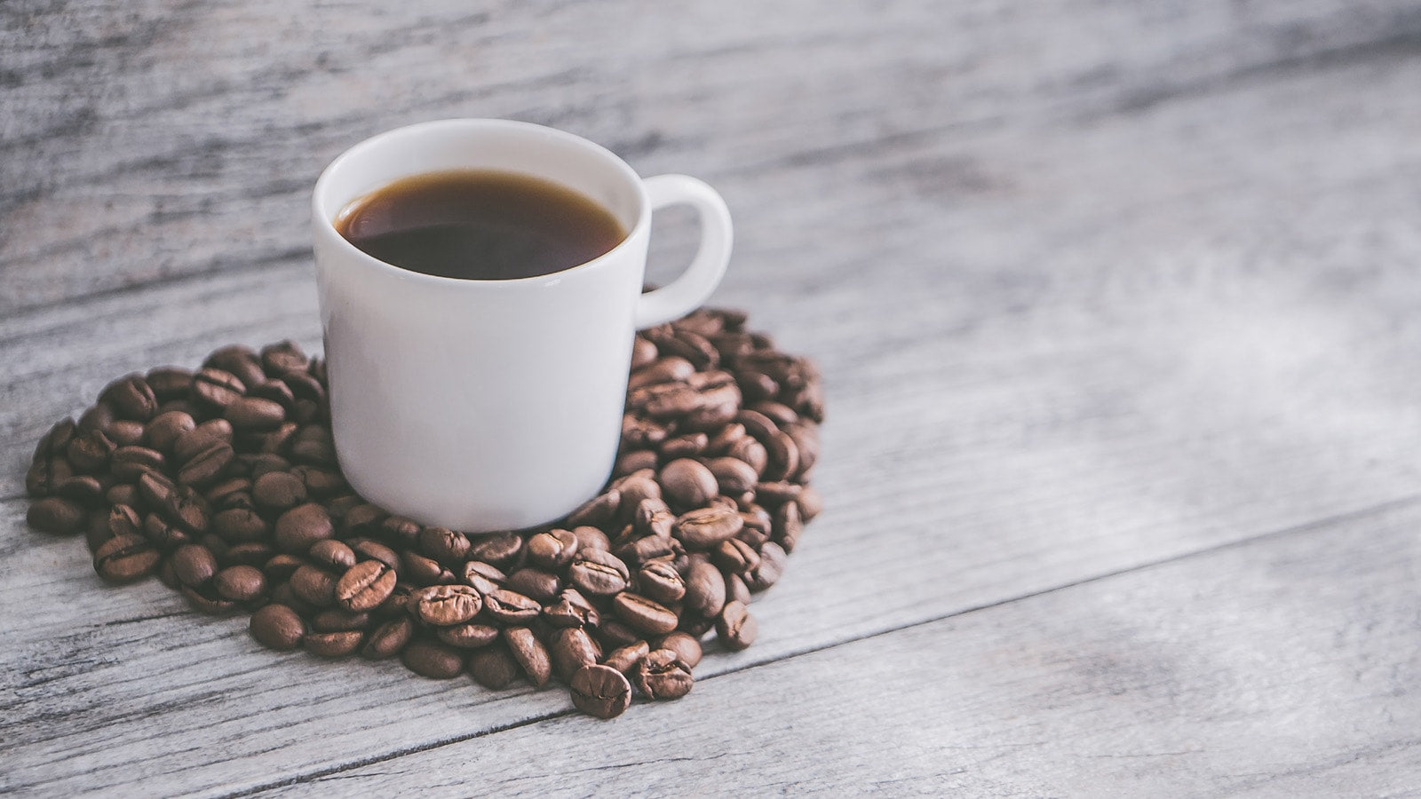 Cup of black coffee amongst coffee beans heart