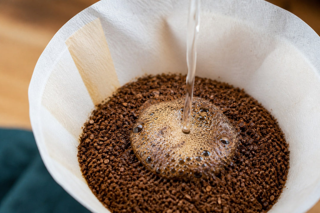Hot water blooming freshly ground coffee inside a white paper filter