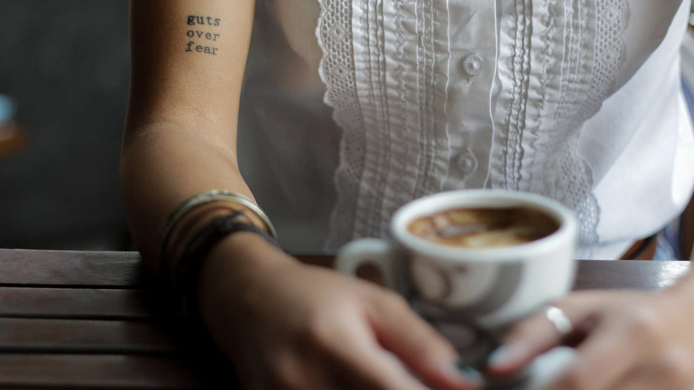 Woman with Guts Over Fear tattoo drinking coffee