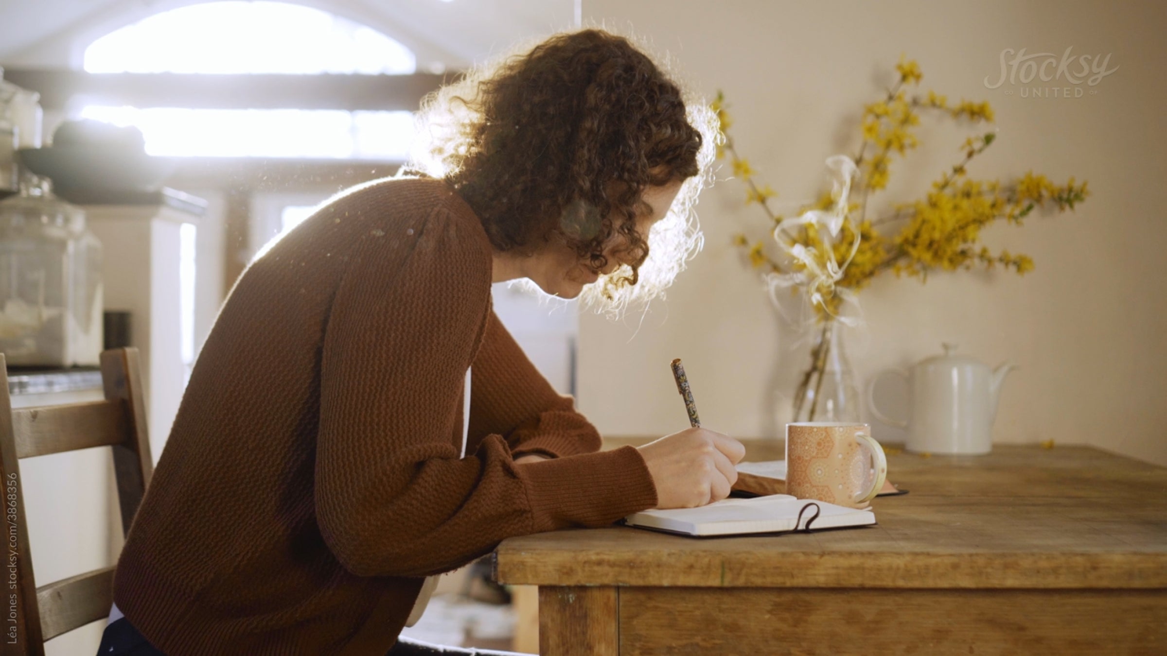 Woman sitting at a desk writing a letter with a cup of coffee.