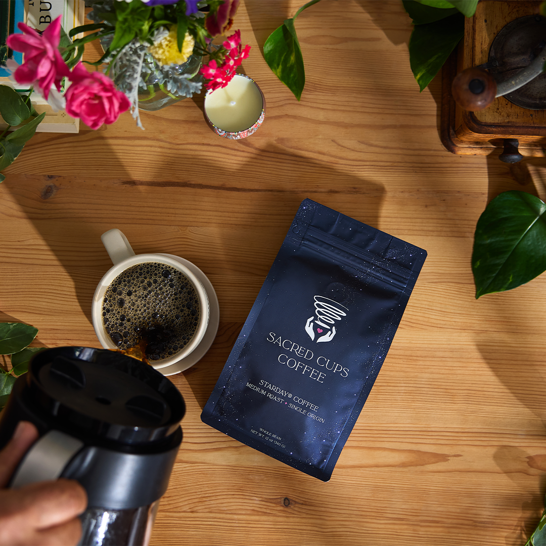 Starday whole bean coffee bag from Purity Coffee styled on a wooden table with a brewed cup of medium roast coffee and flowers